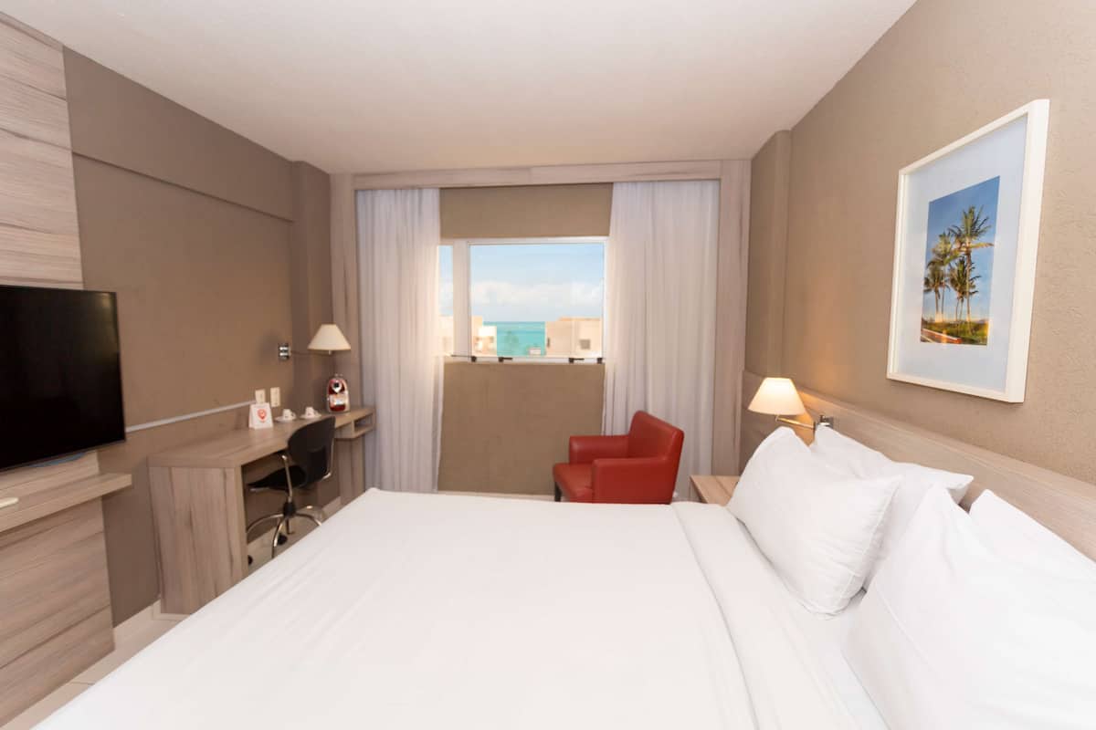 A hotel room with a bed, a desk, a chair, a TV, and a window with curtains.