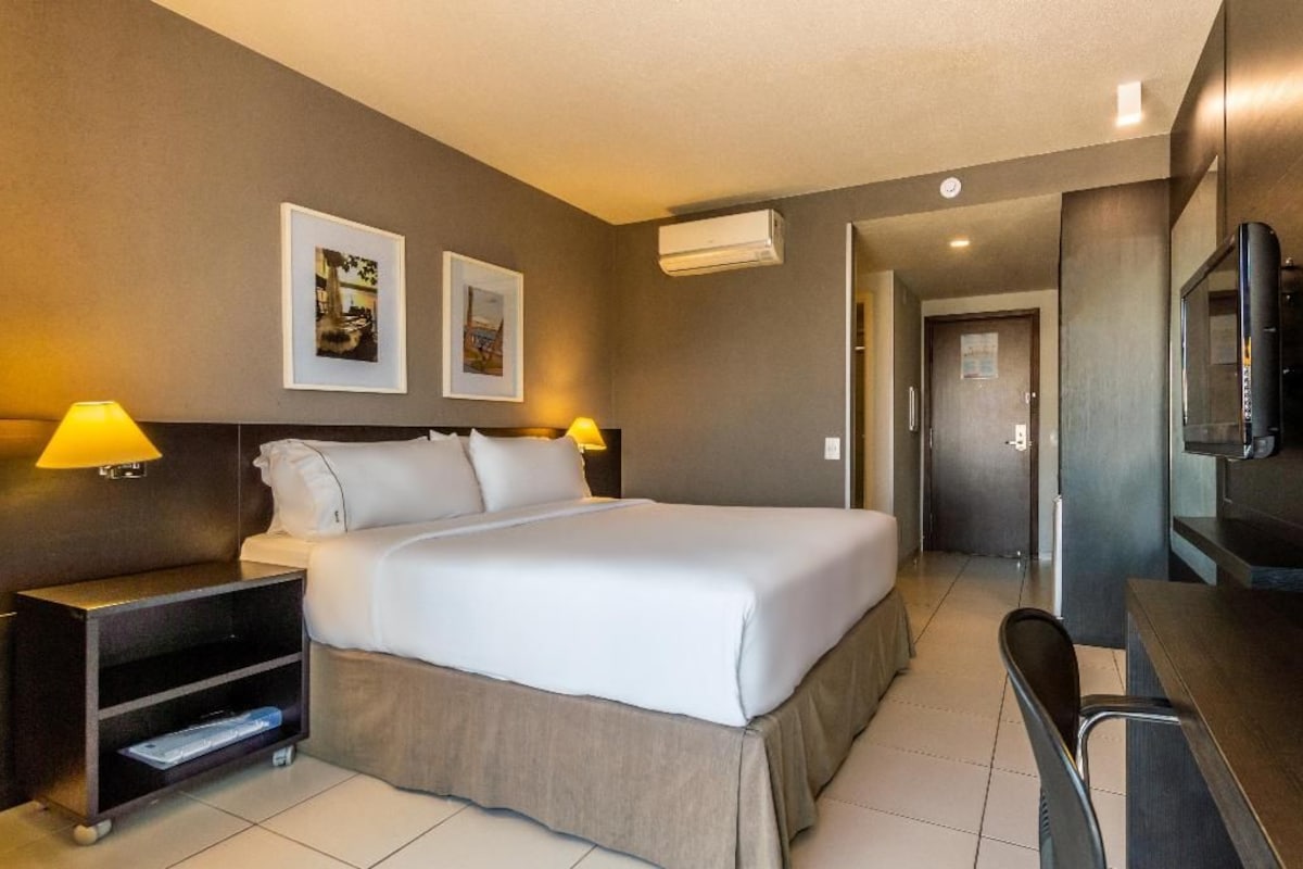 A hotel room with a bed, bedside lamps, a TV, and a desk.
