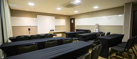 Un salón de conferencias con mesas, sillas, una pizarra y una pantalla de proyección.