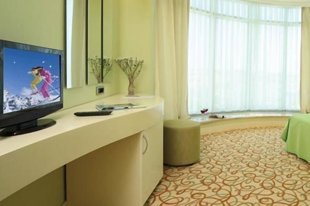 Una habitación de hotel con cama, televisor, escritorio y ventana con cortinas.