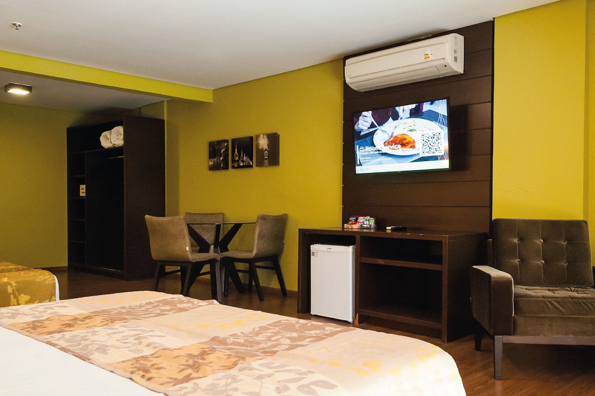 A hotel room with a bed, a desk, two chairs, a television, and a small refrigerator.