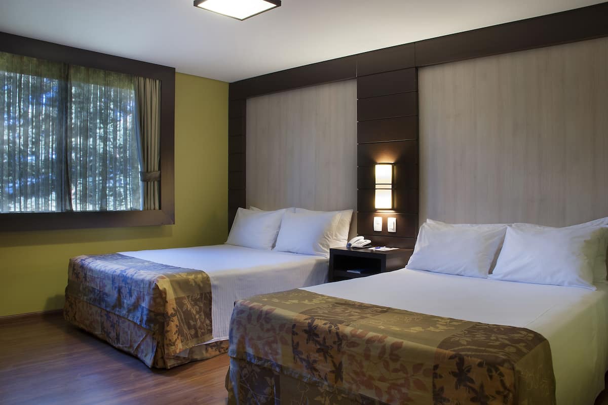 A hotel room with two beds, a nightstand, a lamp, and a window with curtains.