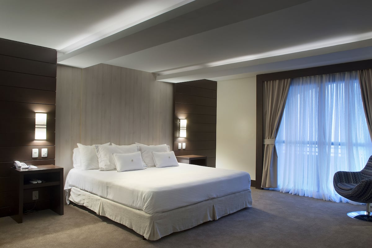 A hotel room with a large bed, bedside lamps, a nightstand, a chair, and a window with curtains.