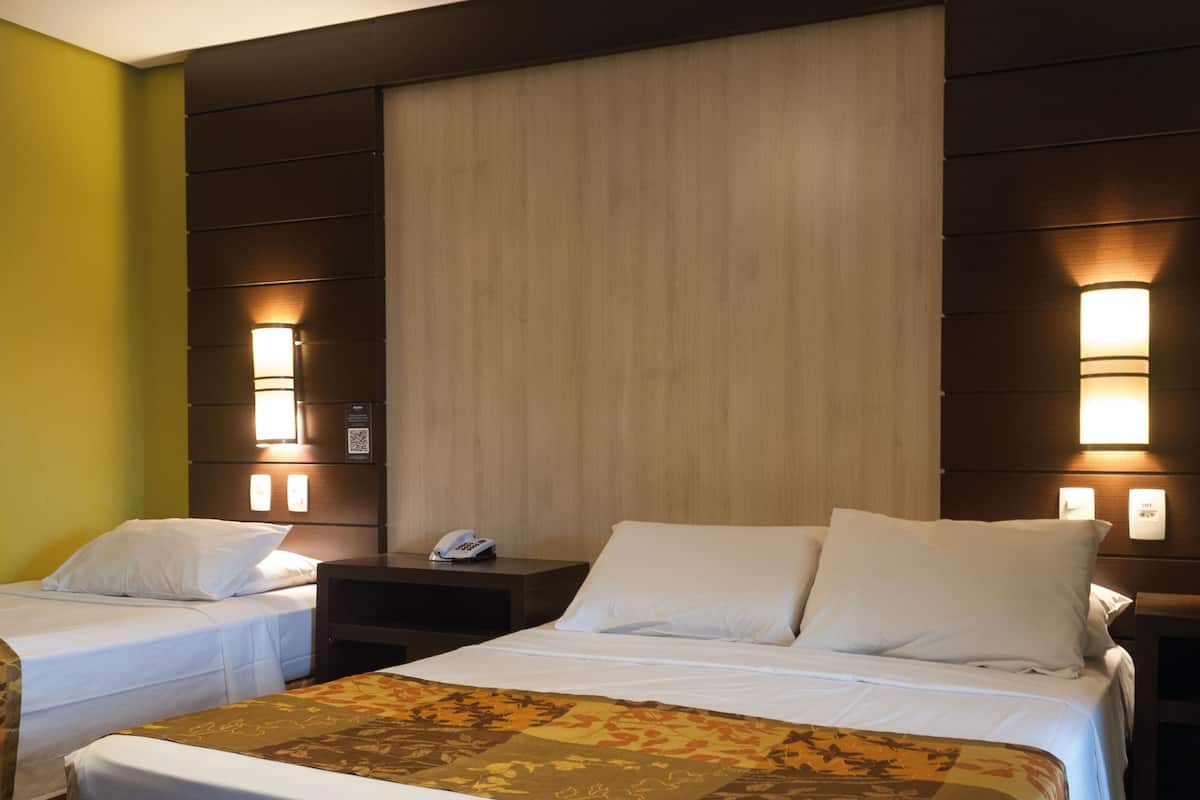 A hotel room with two single beds, a nightstand with a phone, and wall-mounted lights.