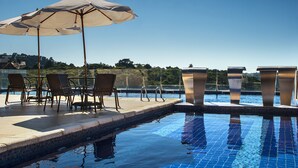 Un espace aménagé au bord de la piscine, avec des chaises longues, un parasol et une vue sur l’eau.