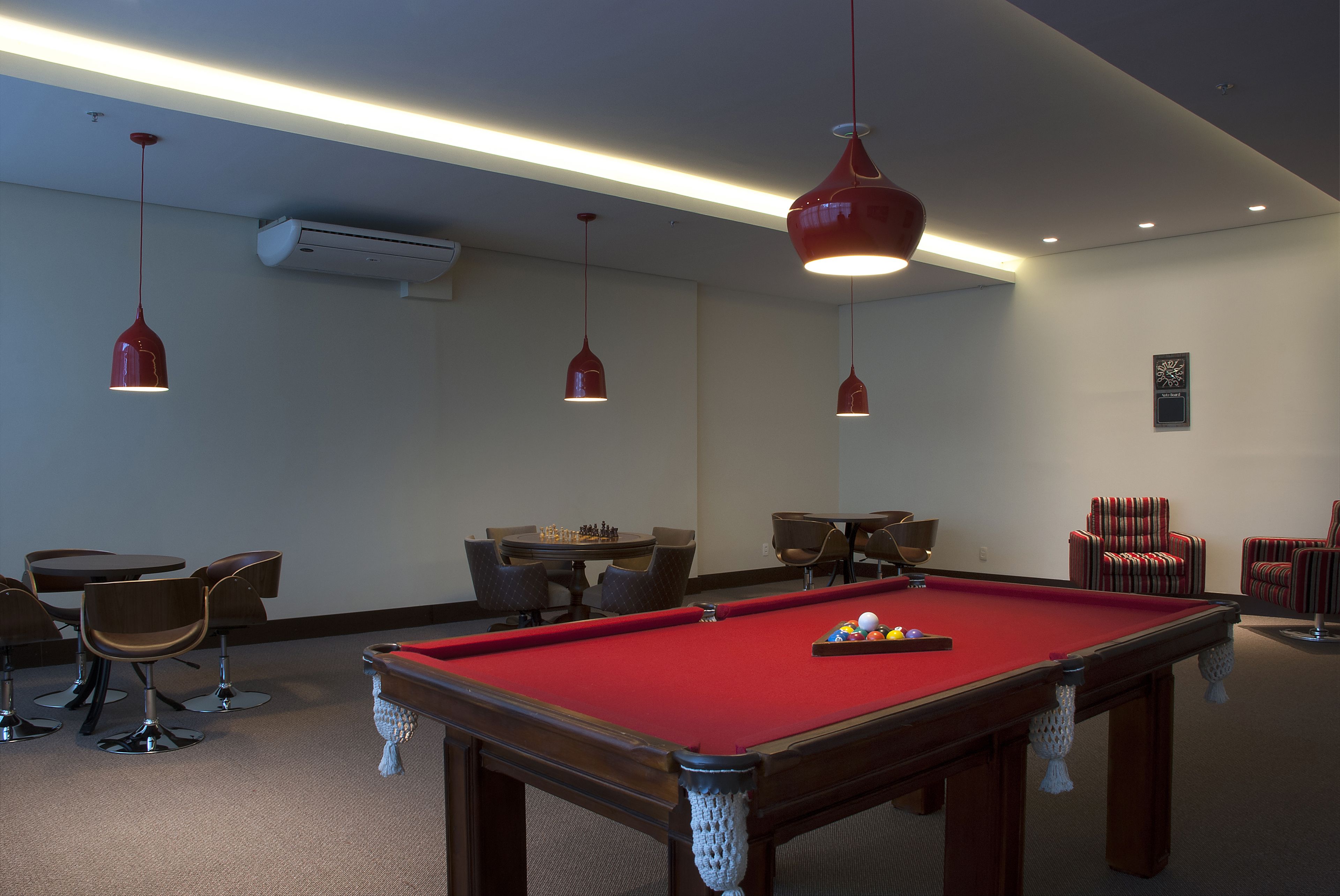 A pool table with a red felt surface, surrounded by brown chairs and a table with a chess set.
