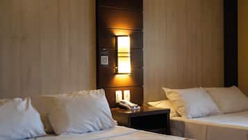 Habitación de hotel con dos camas, una mesita de noche con un teléfono y una lámpara, y un aplique de pared.