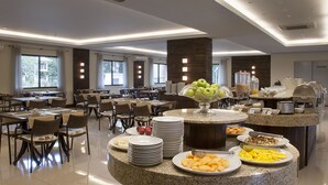 Une salle à manger d’hôtel comprenant plusieurs tables, des chaises et un buffet proposant une variété de plats.