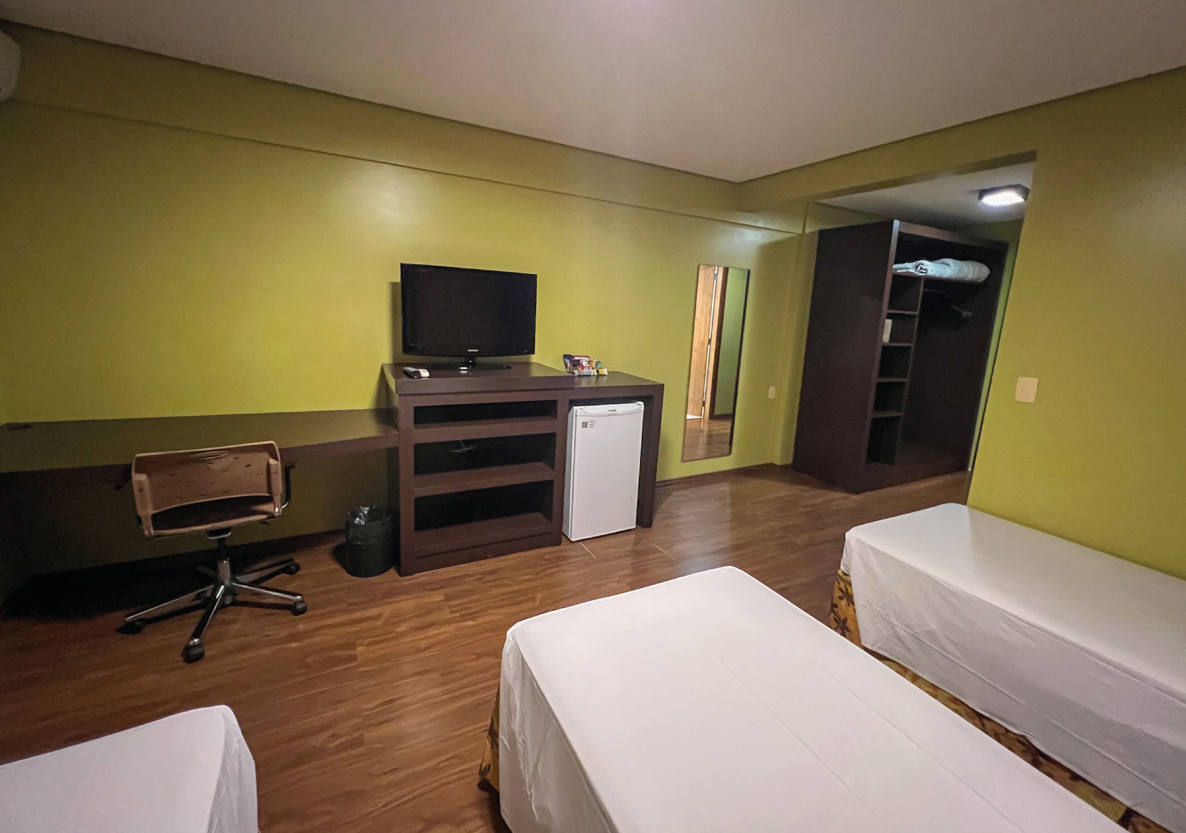 Ein Hotelzimmer mit Schreibtisch, Fernseher, kleinem Kühlschrank, Stuhl, zwei Betten und einem Kleiderschrank.