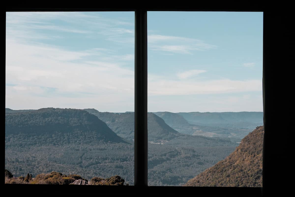 A panoramic view through a window, featuring a mountainous landscape with dense forest coverage and a clear sky.