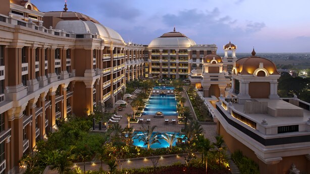 Un hotel con varias plantas, una piscina central y zonas verdes a su alrededor.