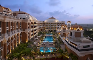 Un hotel con varias plantas, una piscina central y zonas verdes a su alrededor.