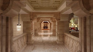 Un gran pasillo con piso de mármol, columnas ornamentales y un candelabro.