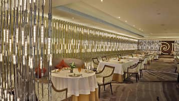 A dining area with round tables, chairs, and a decorative light installation on the wall.