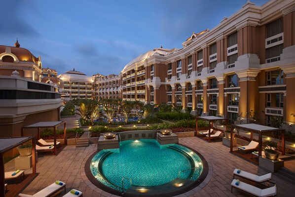 Un área de piscina de hotel con sillones de descanso, un jacuzzi y una gran piscina rodeada de un jardín ajardinado.