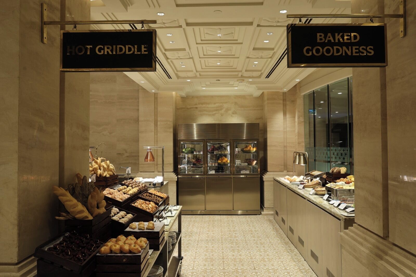 Un espace de petit-déjeuner d’hôtel avec des panneaux indiquant « PLAT CHAUD » et « DÉLICES FRAÎCHEMENT CUITES ».