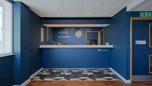 Un área de recepción con un cartel de 'hello & welcome', un reloj y el logotipo de 'Travelodge'.