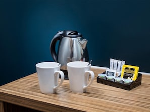 Dos tazas blancas sobre una mesa de madera, con un hervidor plateado y una bandeja de té Twinings.