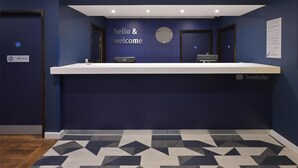 A reception desk with a clock, a 'hello & welcome' sign, and a 'Travelodge' logo.