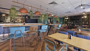 A modern cafe with wooden tables and blue chairs, a bar area, and hanging plants.