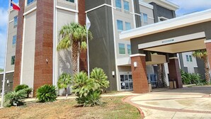 A hotel with a prominent 'Quinta' sign, a covered entrance, and a landscaped front yard with palm trees. - La Quinta Inn & Suites by Wyndham Pearsall (Pearsall)