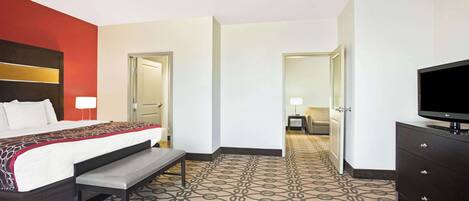 A hotel room with a bed, bench, TV, and a patterned carpet.