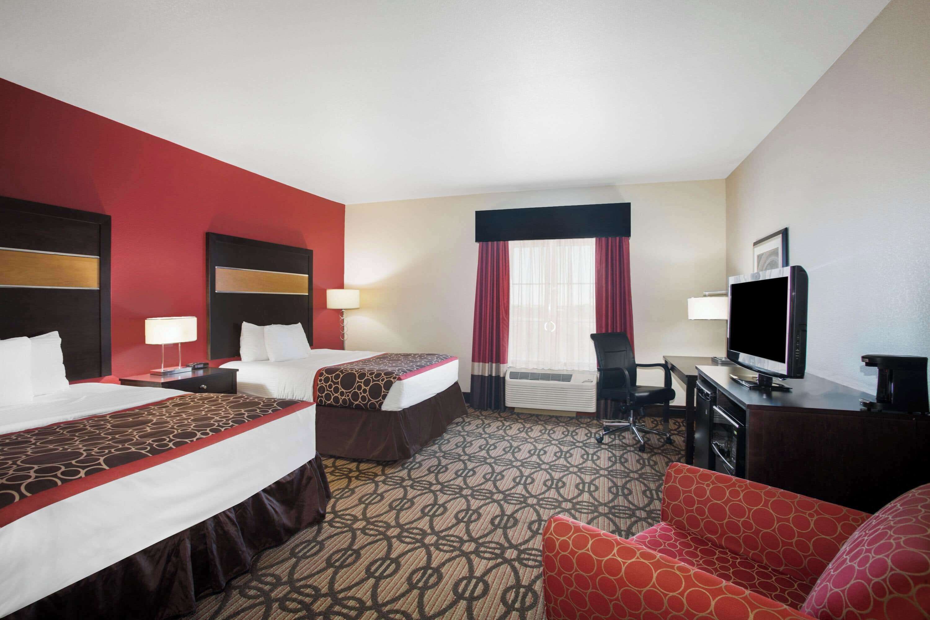 A hotel room with two beds, a desk with a TV, a chair, and a red sofa.