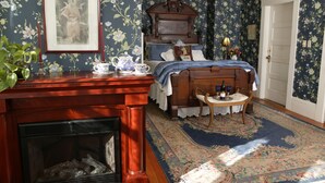 A bedroom with floral wallpaper, a wooden bed, a fireplace, and a nightstand with a vase and candles. - Kelley & Young Wine Garden Inn (Cloverdale)
