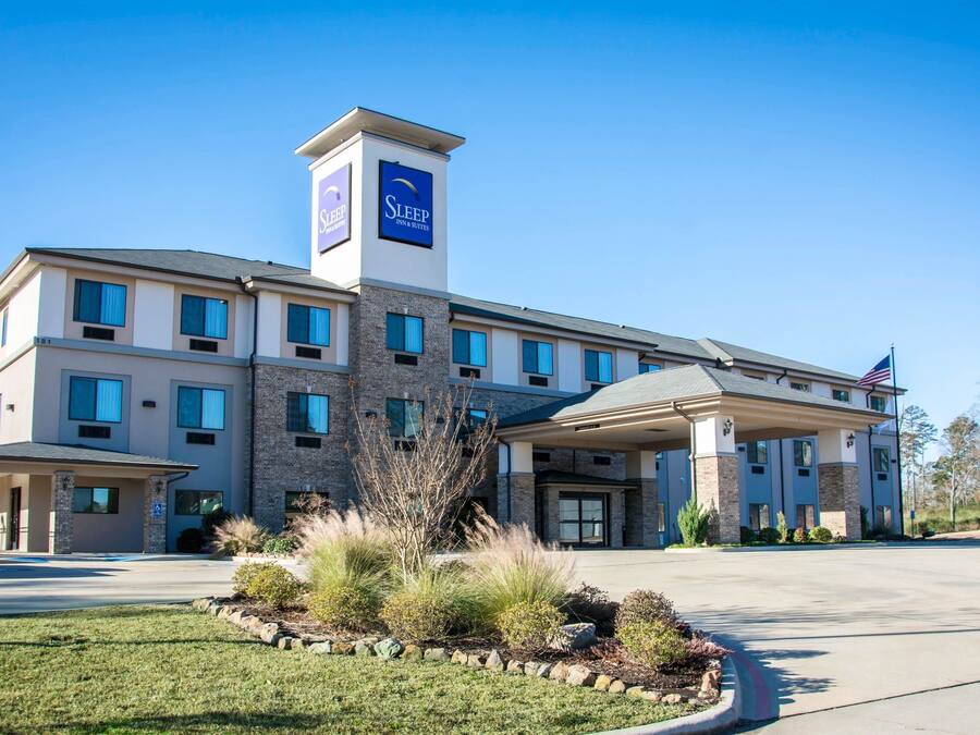 Un hotel Sleep Inn & Suites de diseño moderno, con entrada central, varias ventanas y un césped bien cuidado.
