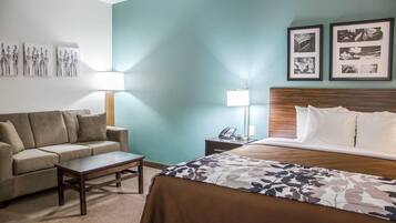 A hotel room with a bed, a sofa, a coffee table, a nightstand with a lamp, and wall art.