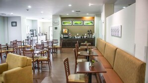 Ein Restaurant mit mehreren Tischen und Stühlen, einer Theke mit einer Kaffeemaschine und gerahmten Bildern an der Wand.