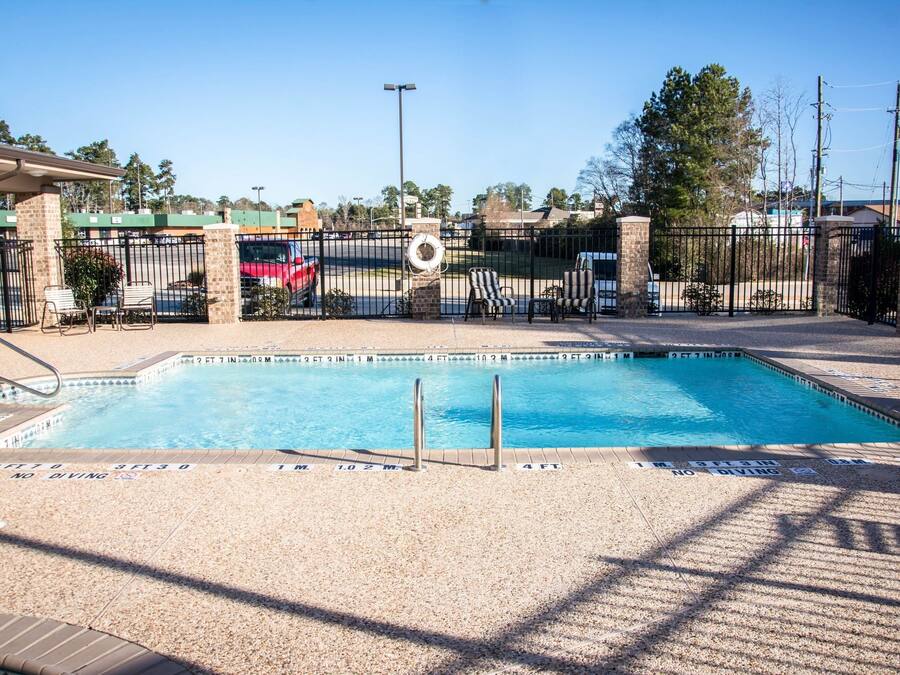 Piscina rectangular con un cartel de prohibido bucear, rodeada por una valla y sillas.