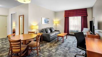 Habitación de hotel con una mesa de comedor, sillas, un sofá, un televisor y una lámpara.