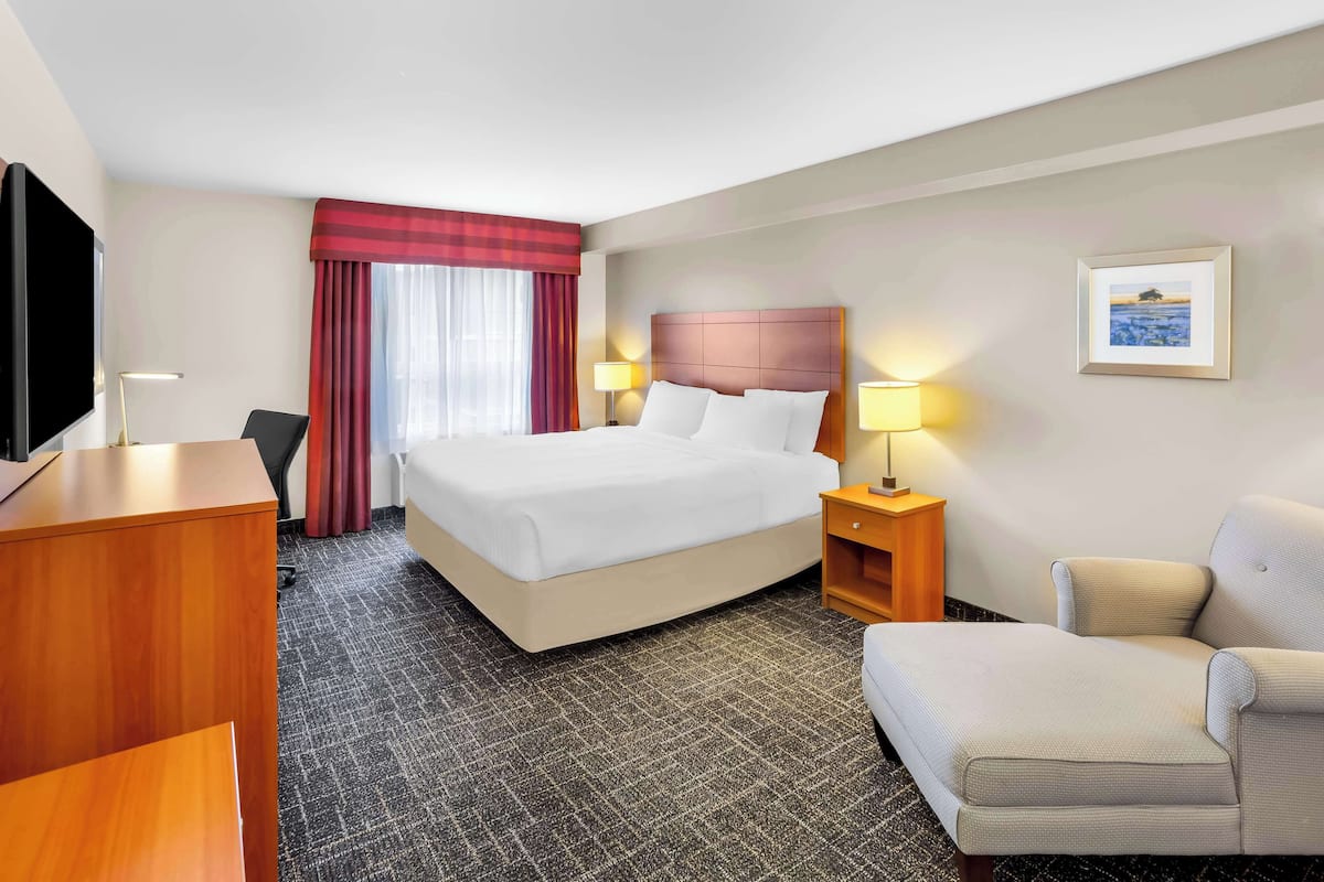 A hotel room with a bed, a desk, a chair, a TV, and a picture on the wall.