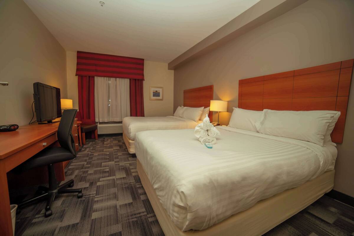 A hotel room with two beds, a desk with a chair, a television, and a window with curtains.