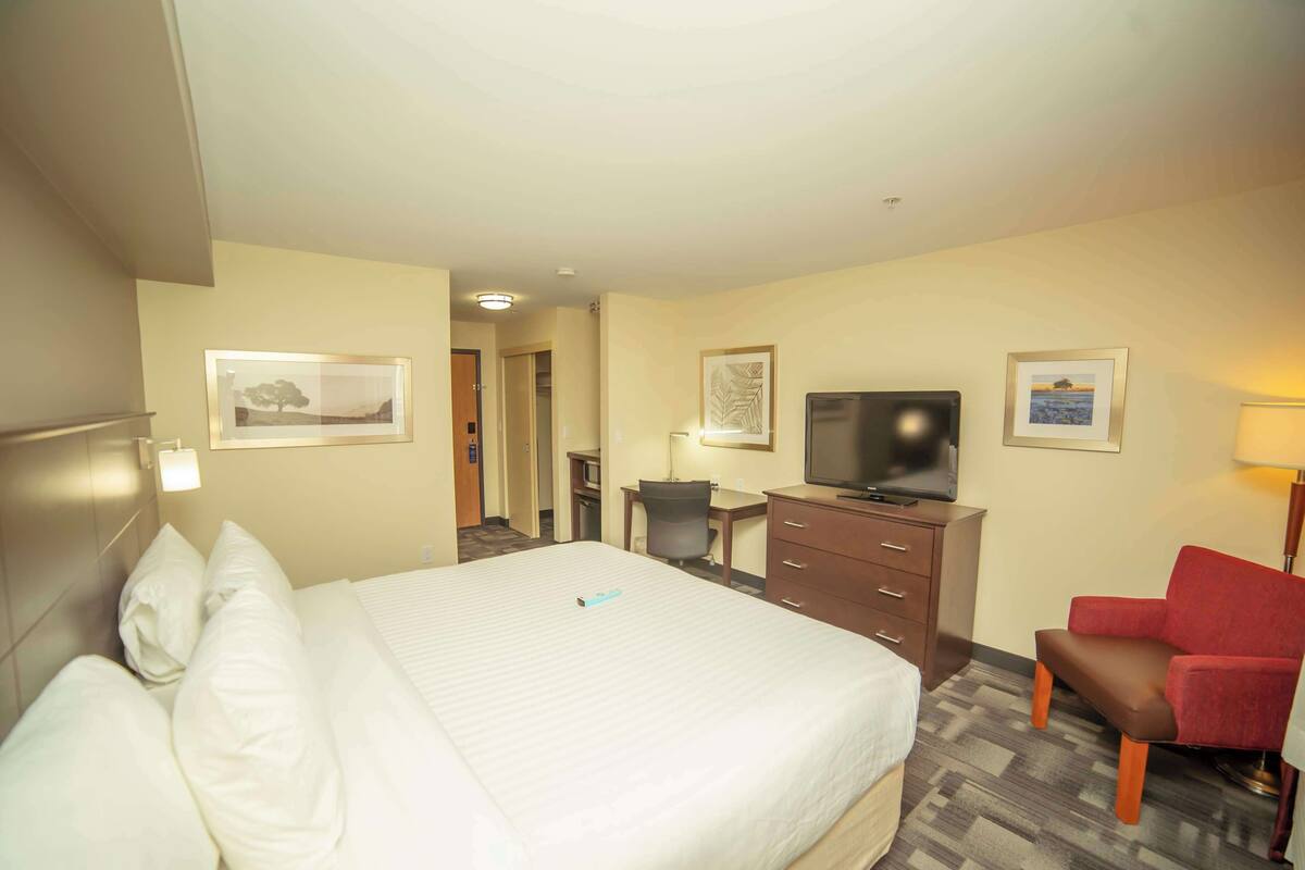 A hotel room with a large bed, a desk with a computer, a television, and a red chair.