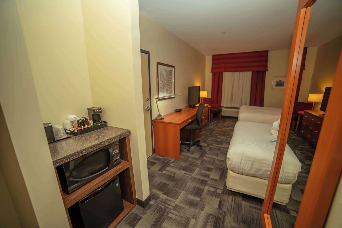A hotel room with a bed, a desk with a chair, a microwave, a small refrigerator, and a television.
