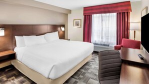 Hotellihuone, jossa on suuri sänky, työpöytä tuolilla, televisio ja ikkuna, jossa on verhot.