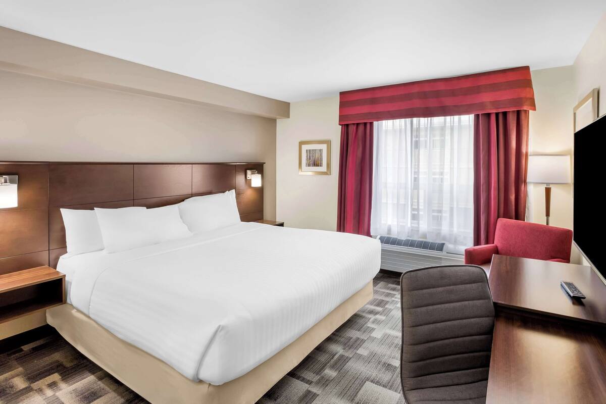 A hotel room with a large bed, a desk with a chair, a TV, and a window with curtains.
