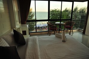 A hotel room with a large window offering a view of a beach and a balcony with wicker chairs and a table. - Magic House Hostel (Cha-am)