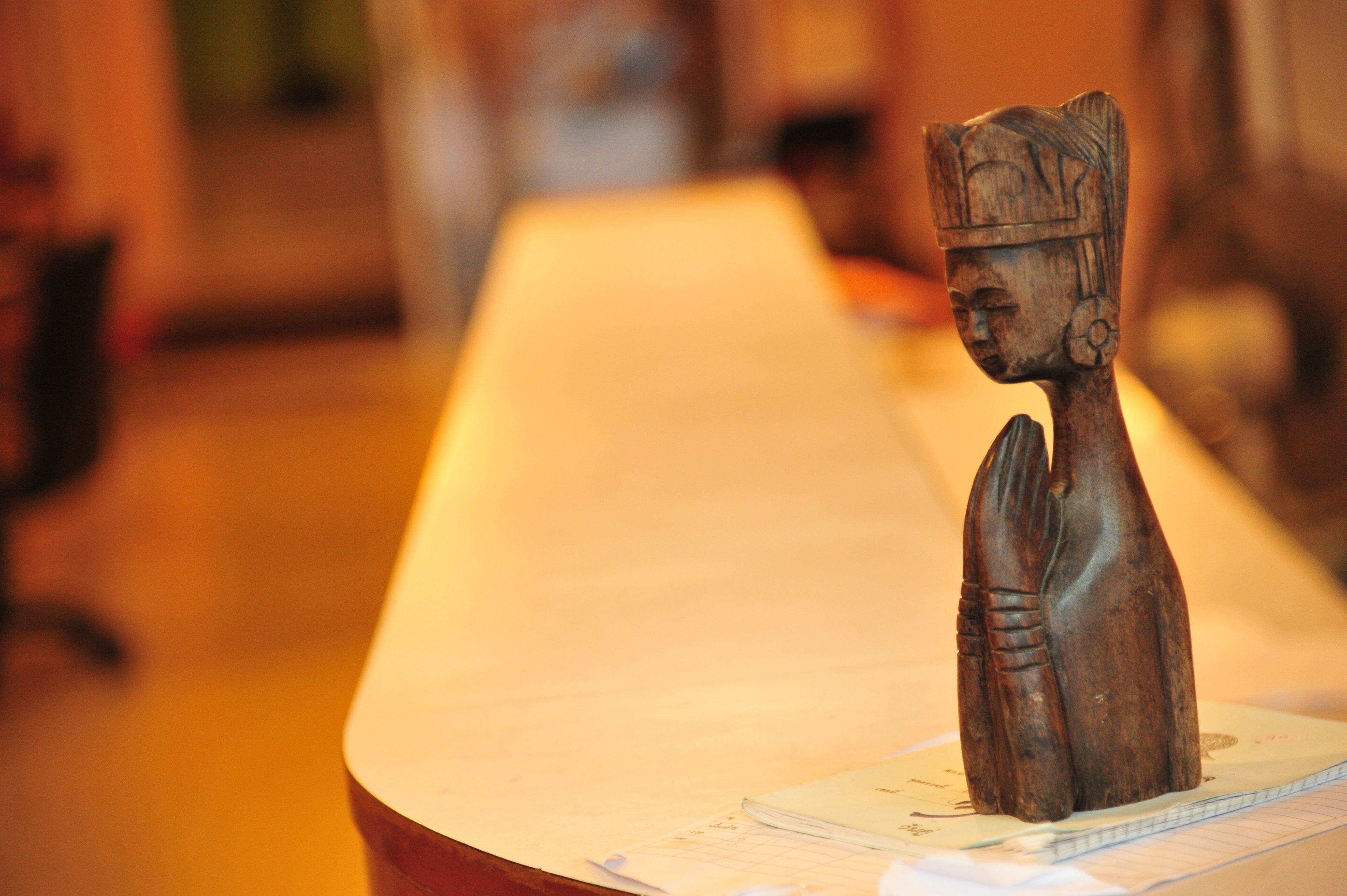 A wooden sculpture on a table with a notebook and pen beside it.