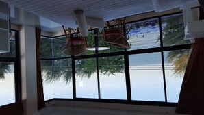 A room with large windows, wicker baskets hanging from the ceiling, and a view of a lake. - Magic House Hostel (Cha-am)