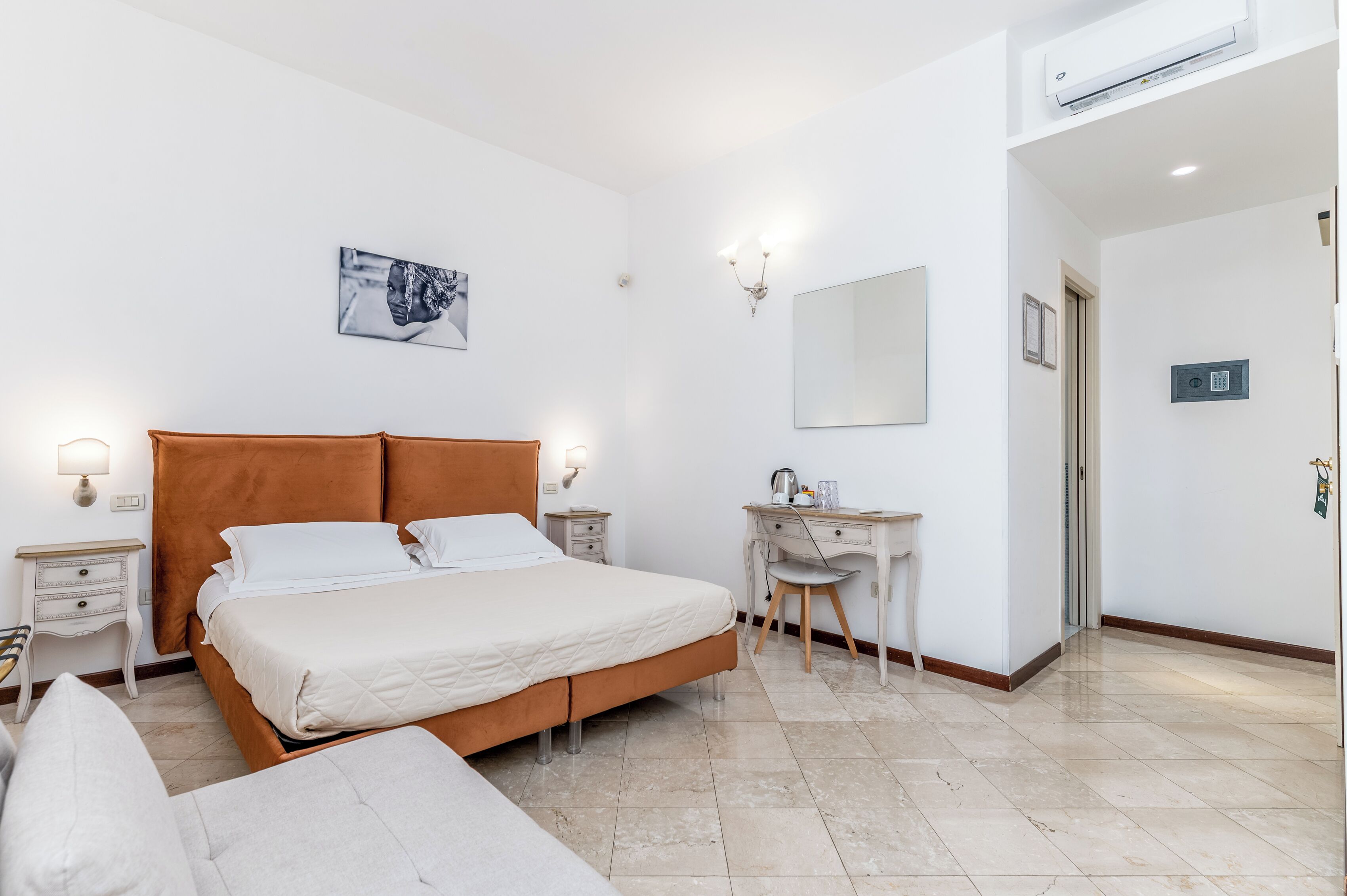 Une chambre à coucher comprenant un lit, des tables de chevet, un bureau, une chaise, un miroir et un climatiseur fixé au mur.