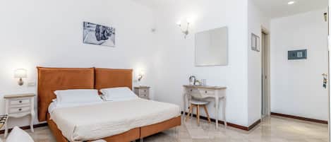 Une chambre à coucher comprenant un lit, des tables de chevet, un bureau, une chaise, un miroir et un climatiseur fixé au mur.