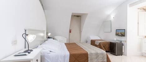 A modern hotel room with a large bed, a desk, a chair, a TV, and a small kitchenette.