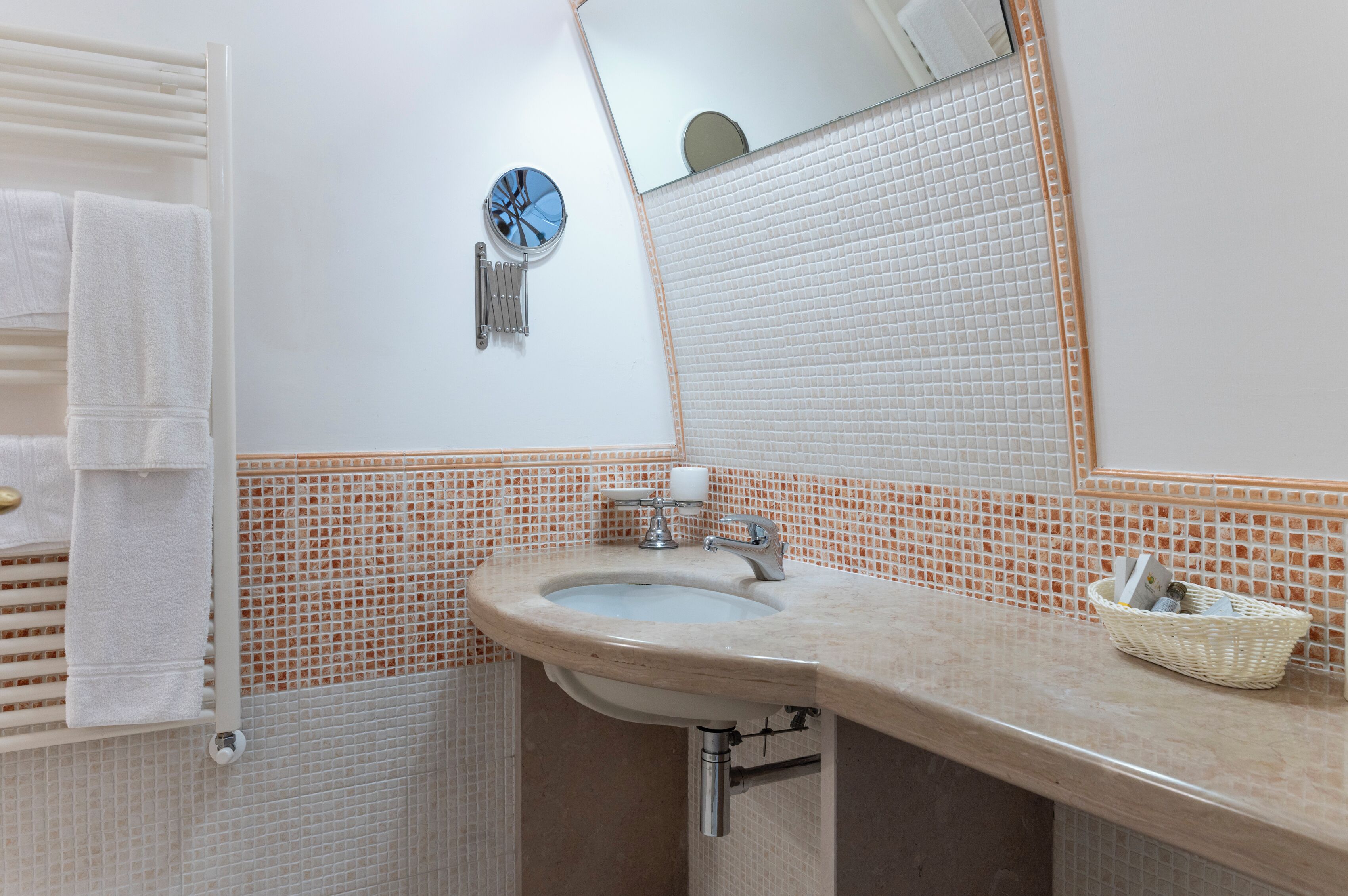 Un baño con lavamanos, espejo, toallero y una pequeña cesta en la encimera.