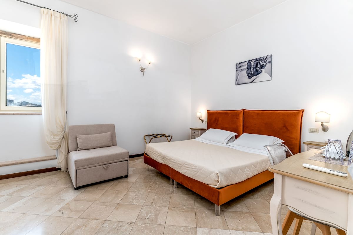A bedroom with a bed, a sofa, a desk, and a window with curtains.
