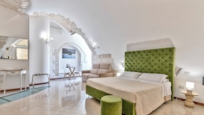 A modern hotel room with a large bed, a green ottoman, a desk, and a chair. - Hotel La Terra (Ostuni)
