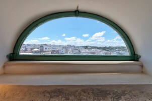 Vista a través de una ventana con marco verde, que muestra un paisaje urbano con edificios y cielo despejado.
