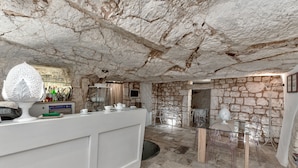 A stone-walled kitchen with a white countertop, a glass table, and clear chairs. - Hotel La Terra (Ostuni)